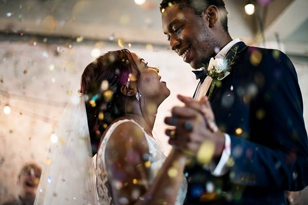 newly wed black man and woman dancing, smiling at each other, with glittery confetti in foreground