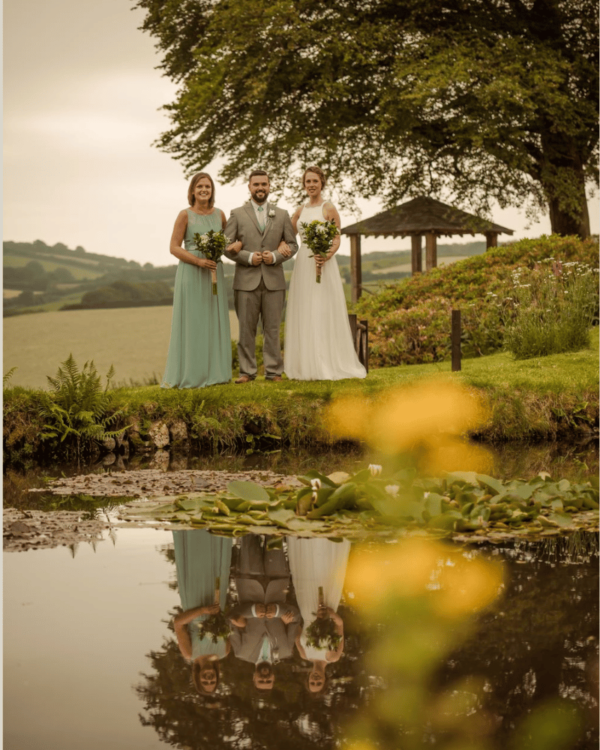 wedding party standing by countryside pond