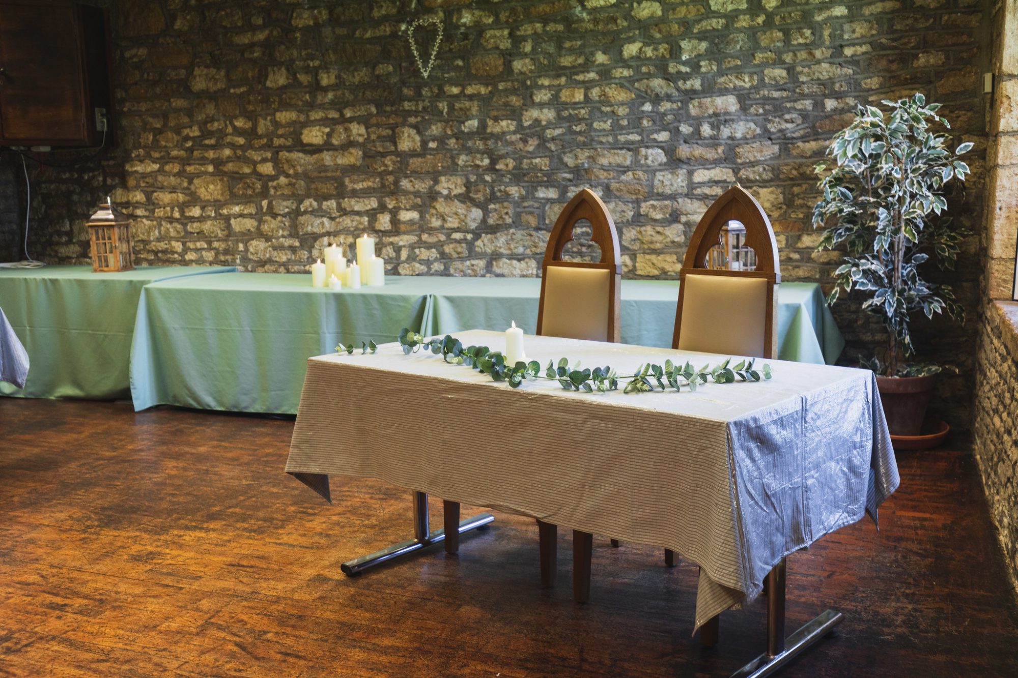 wedding ceremony setting - table with white cloth and leaves and candle, with 2 medieval style chairs behind. Bare stone walls in background