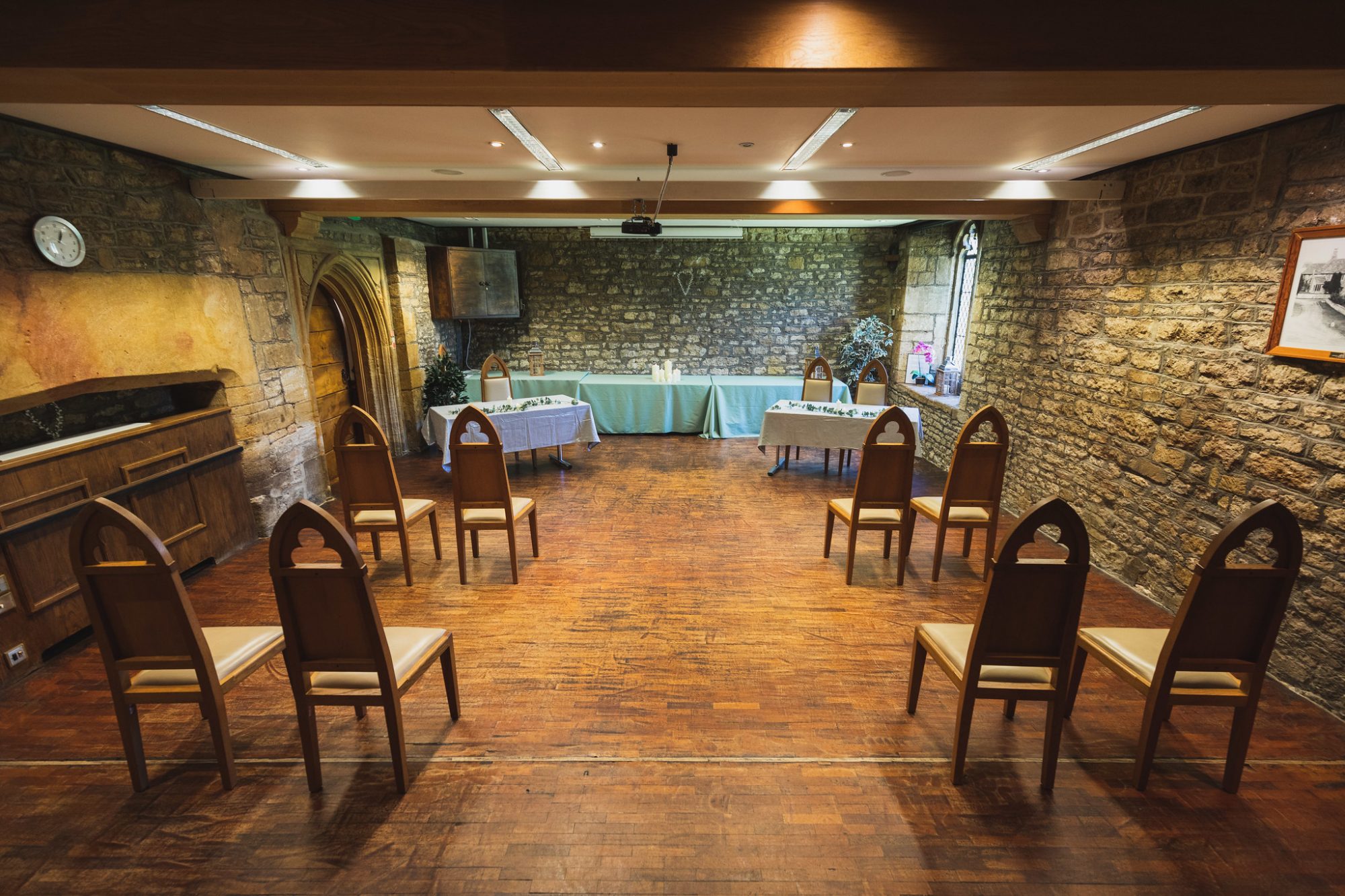 ceremony room with old bare stone walls, medieval style chairs either side of a wood floored aisle.