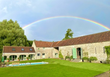 converted stone barn buildings with lawn and swimming pool in foreground and rainbow overhead